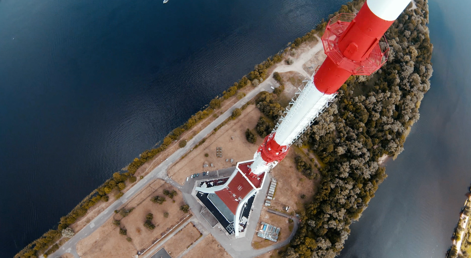 Aerial view of a red and white lighthouse tower against dark waters and rocky coastline.