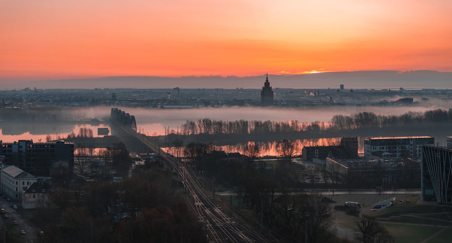 Wide panoramic view of a city skyline at sunset with golden light reflecting off buildings and water.