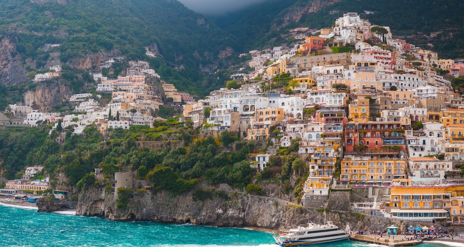 Colorful Mediterranean coastal town built into steep hillside with traditional architecture and blue water below.