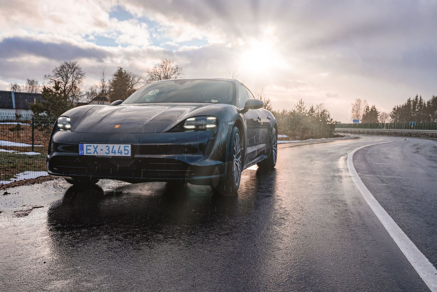 Porsche Taycan reflected in puddles during dramatic cloudy sunset on empty street.
