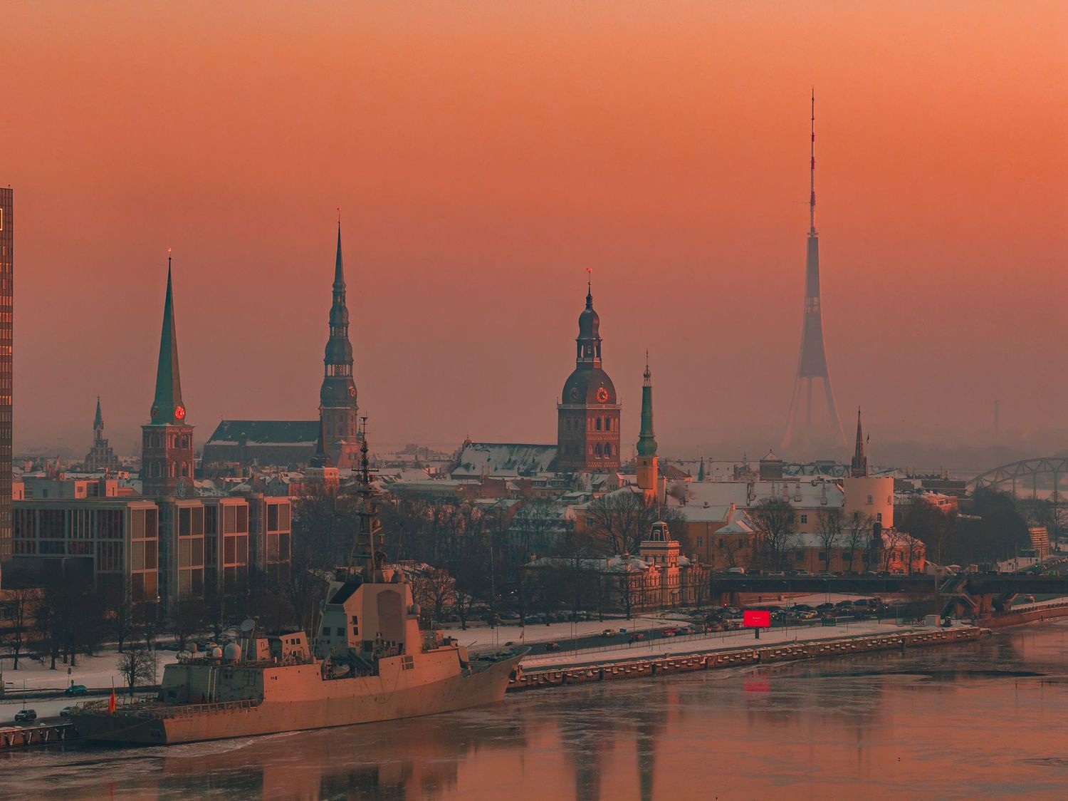 Panoramic cityscape of Hamburg's historic skyline with church spires silhouetted against an orange sunset sky.