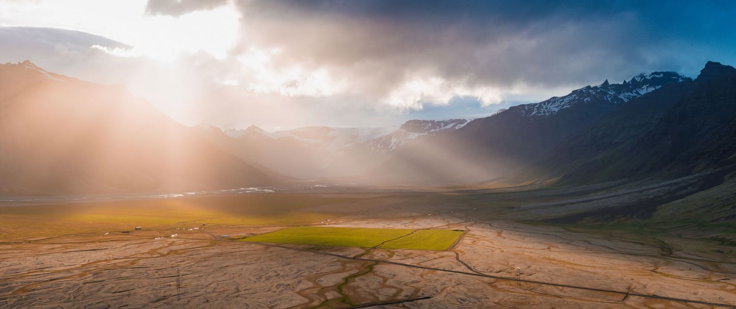 Golden sunbeams pierce through clouds over a mountainous valley at sunset.