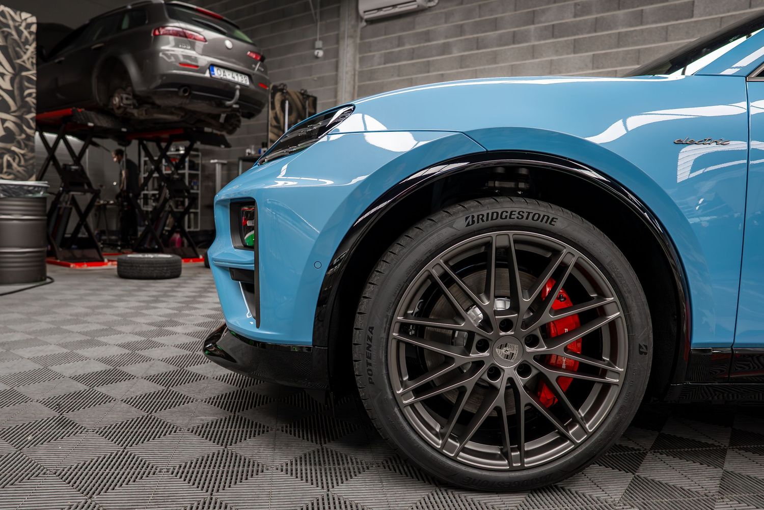 Low angle shot of light blue sports car wheels with red brake calipers and black alloy rims.
