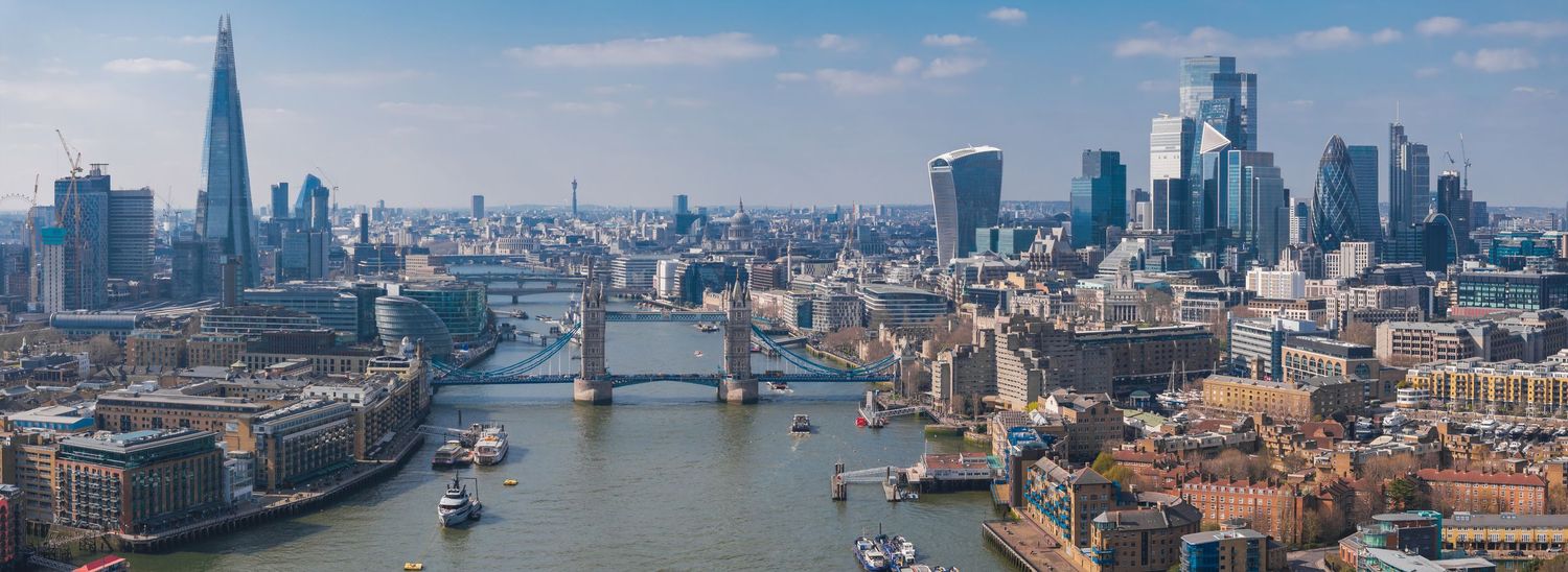 Panoramic view of London skyline featuring the Shard and other modern buildings along the Thames River.