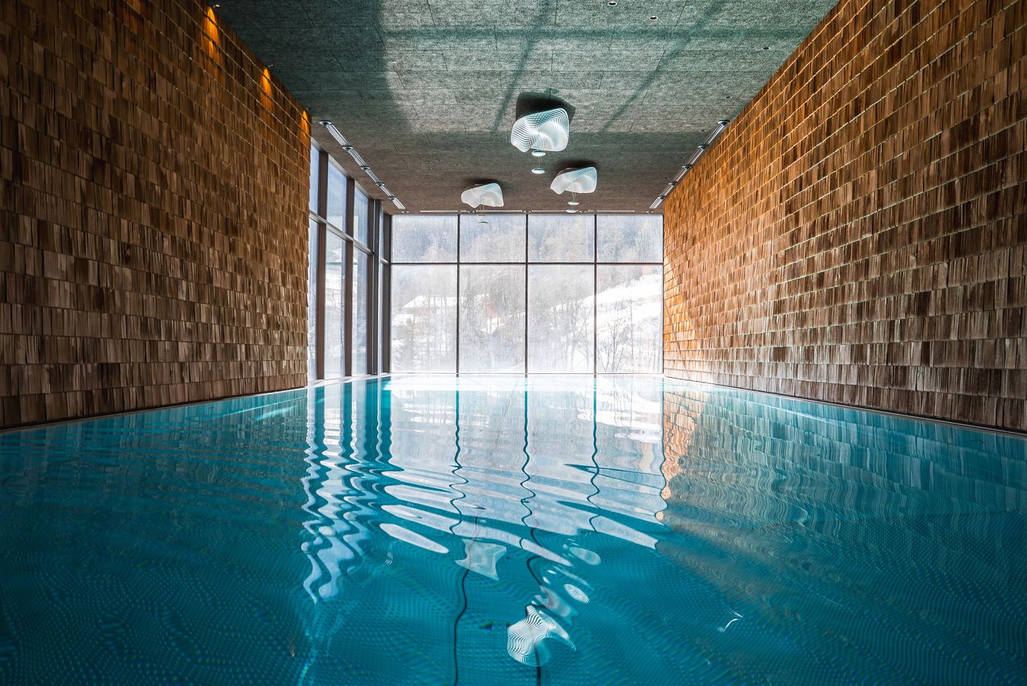 Long indoor swimming pool with brick walls and natural light streaming through windows.