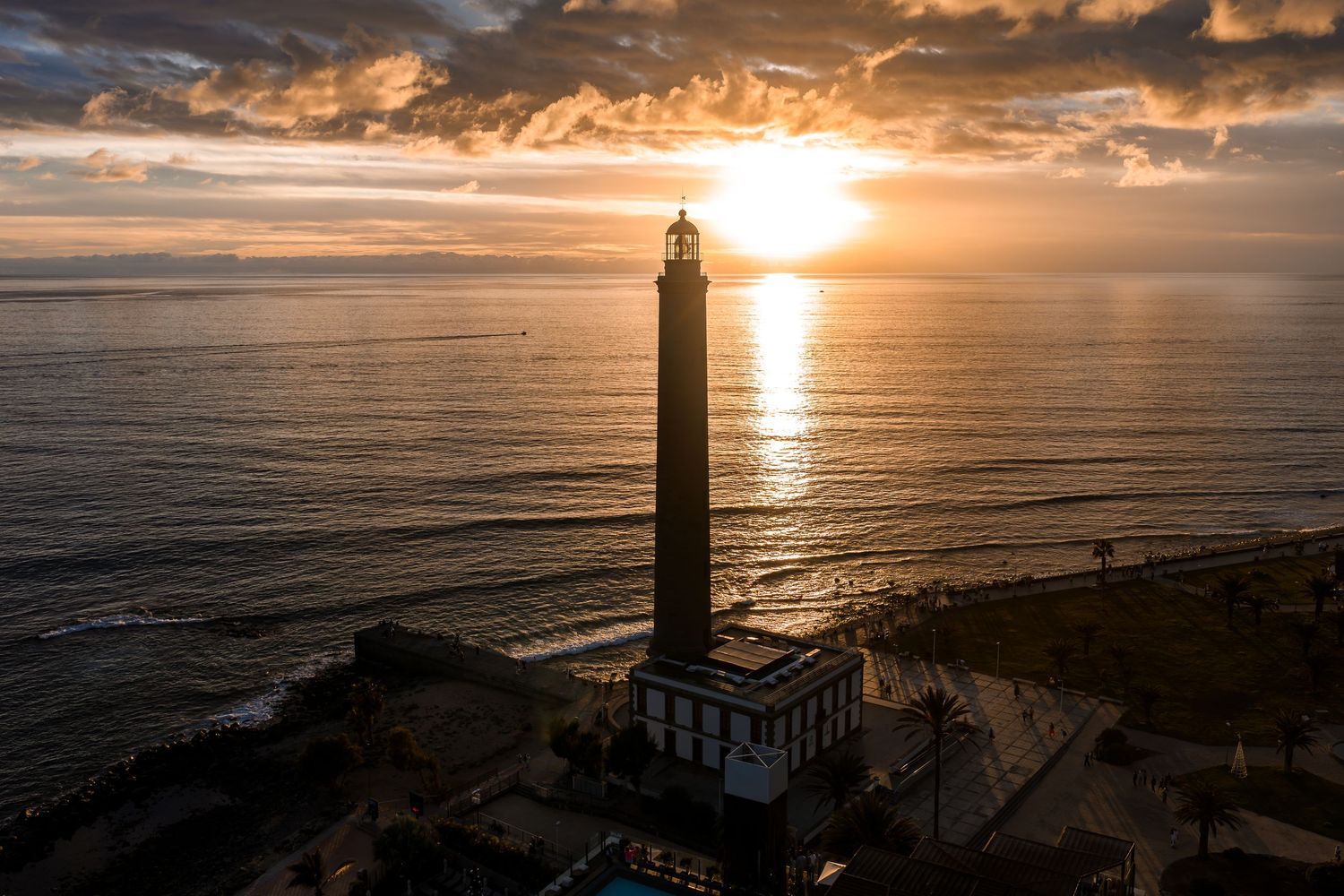 Dramatic sunset over a lighthouse on the coast with golden clouds reflecting on the ocean waters.