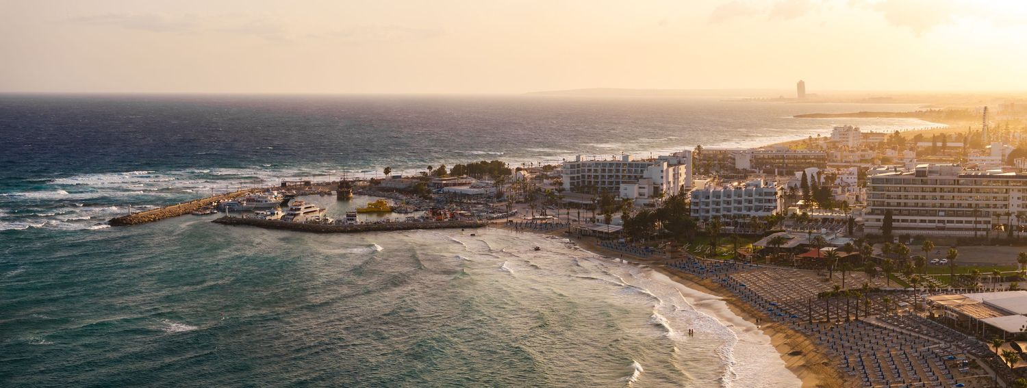 Golden sunset panorama over coastal city with beach and urban development along shoreline.