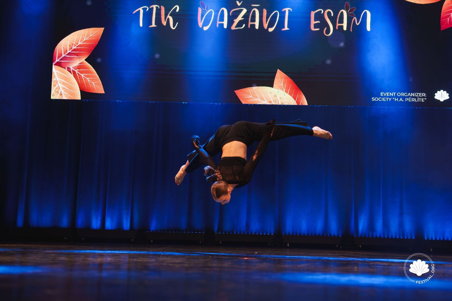 Modern dance performance on stage with deep blue lighting and projected text elements.