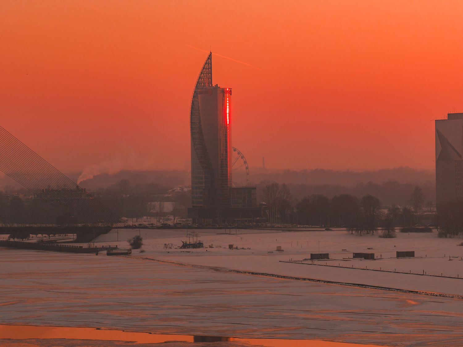 Silhouetted boats float in calm waters against an orange sunset sky with city skyline in the background.
