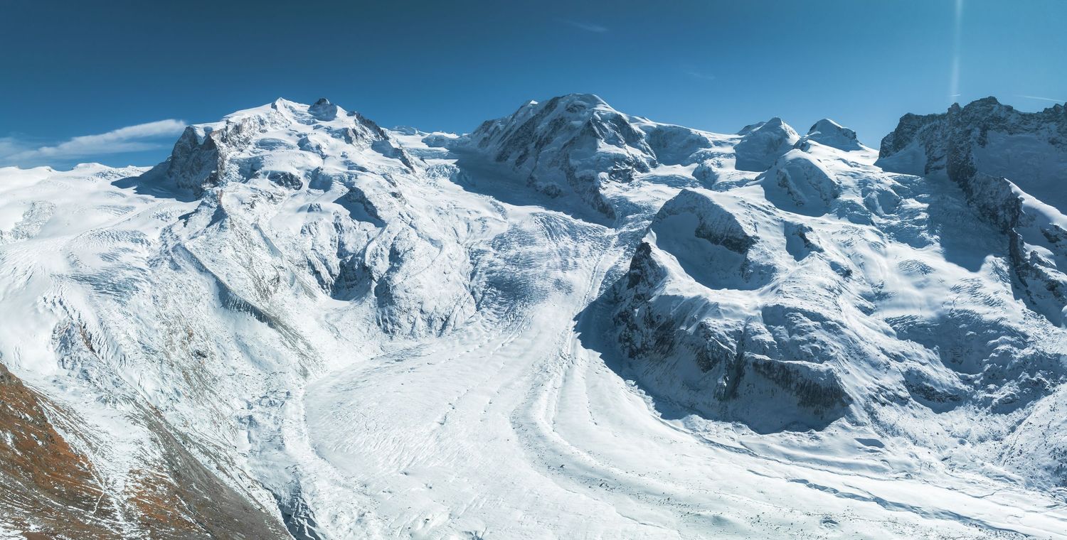 Dramatic vista of snow-covered Alpine peaks and glaciers under bright blue sky.
