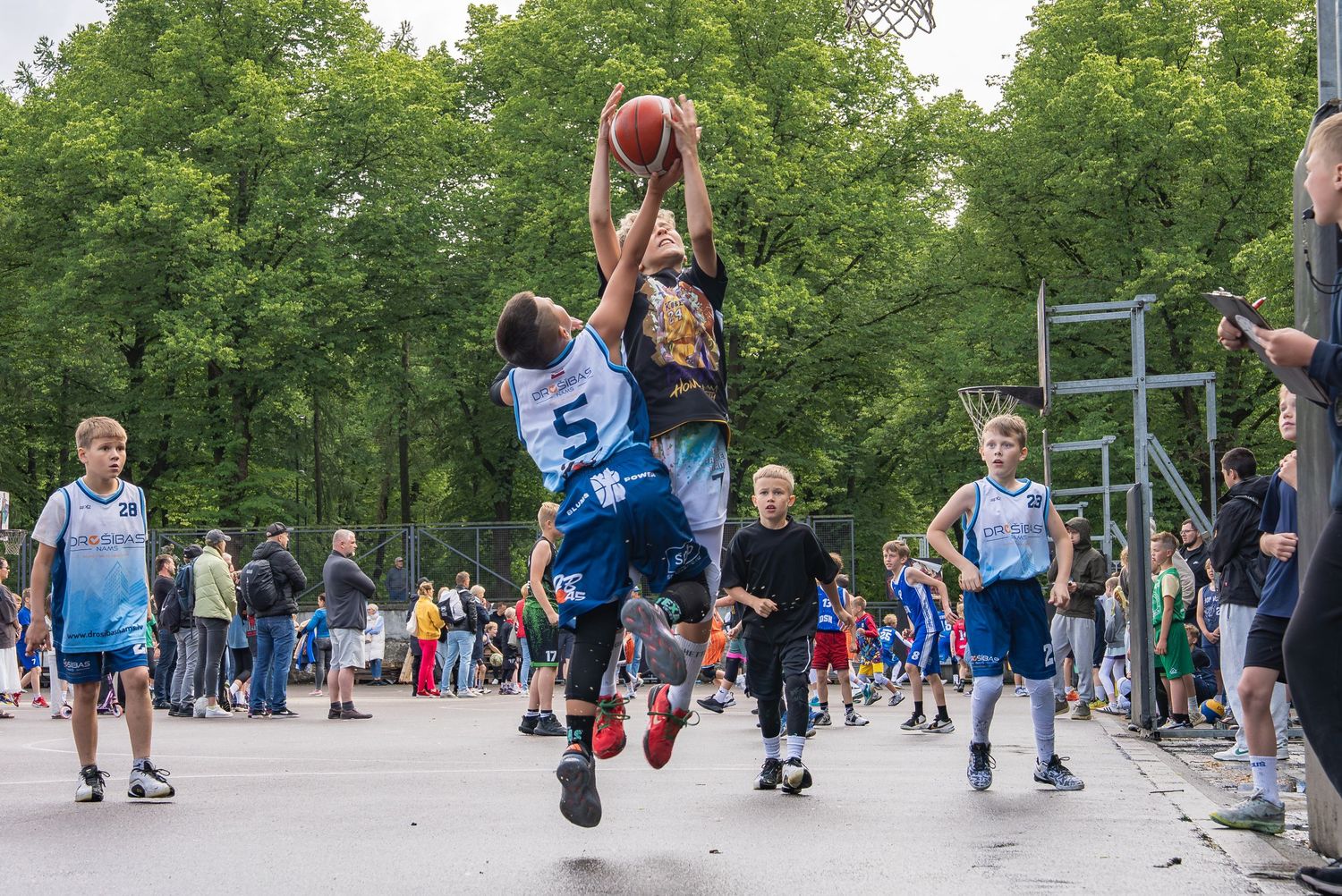 Wide view of skateboarders performing at an outdoor park with spectators watching.