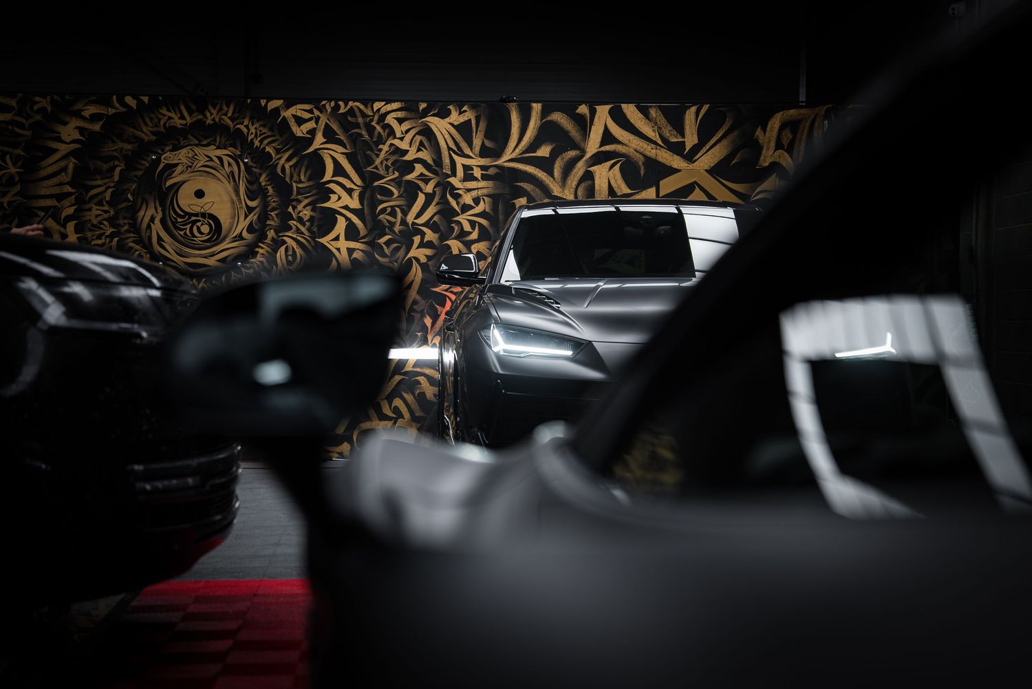 Dark automotive showroom with elegant sports cars and ornate wallpaper details.