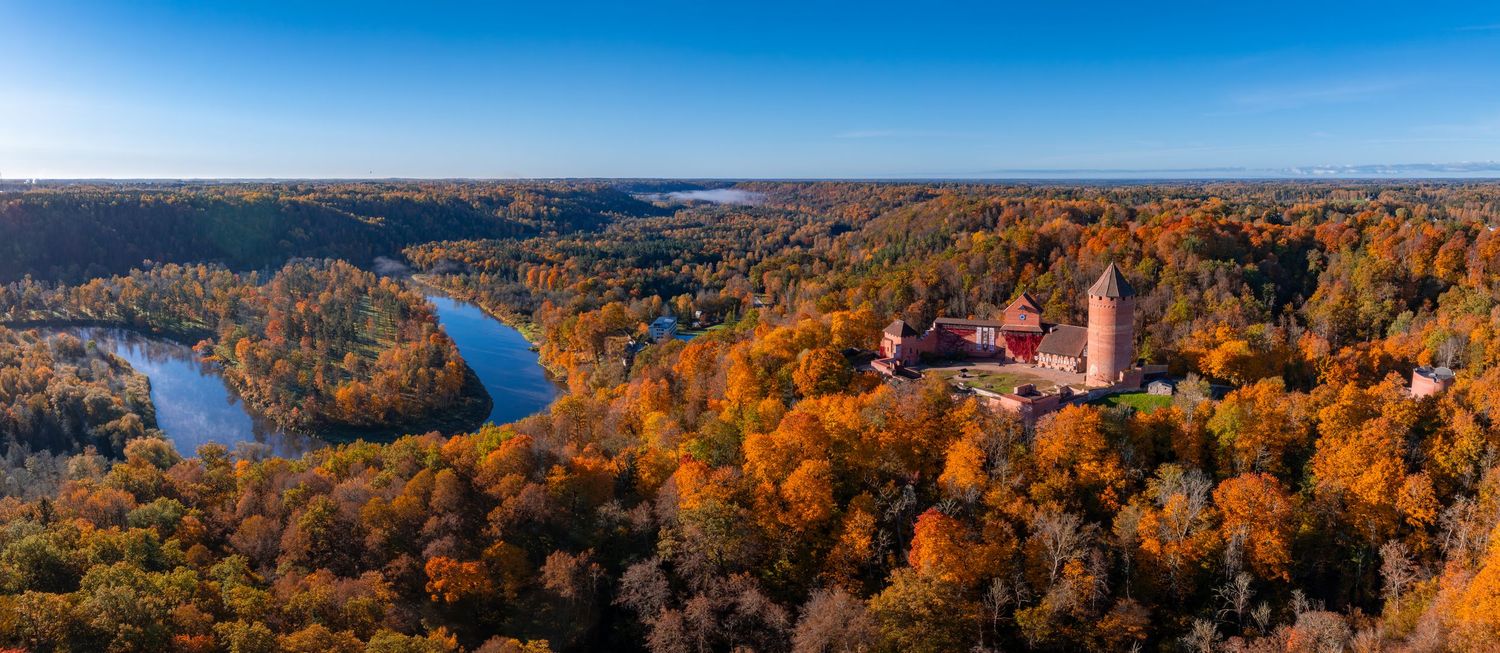 Panoramic autumn landscape showing colorful fall foliage around lake and mountains.