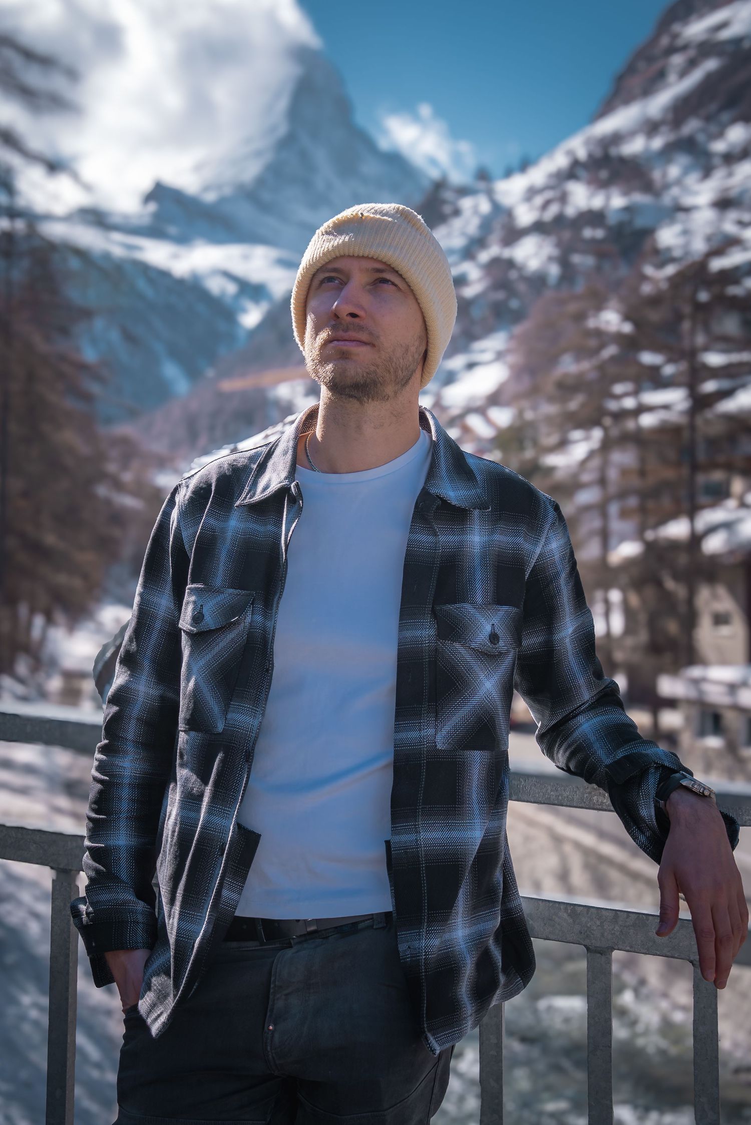 Winter mountain landscape with snow-covered peaks and person in plaid jacket resting on railing.