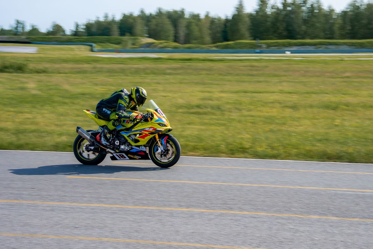 Yellow and black sportbike racing along an empty track on a sunny day.