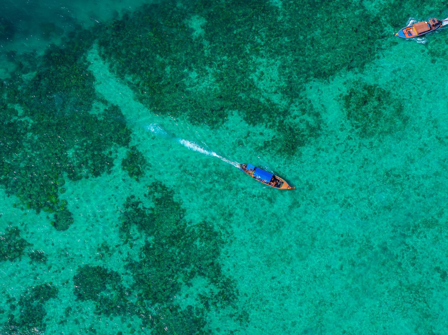 Aerial view of boats floating over vibrant turquoise coral reefs in tropical waters.