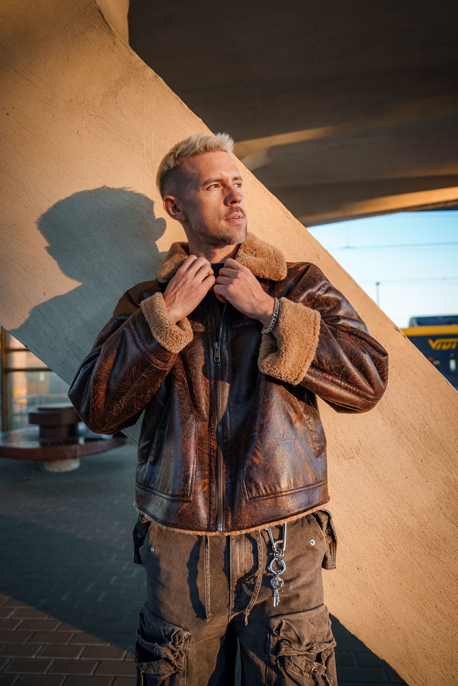 Person in brown leather jacket posing against concrete wall in dramatic lighting sequence.