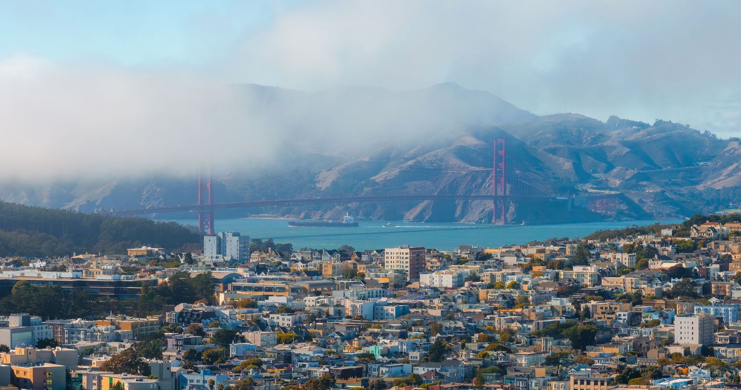Panoramic cityscape view of San Francisco Bay Area with mountains and fog in the distance.