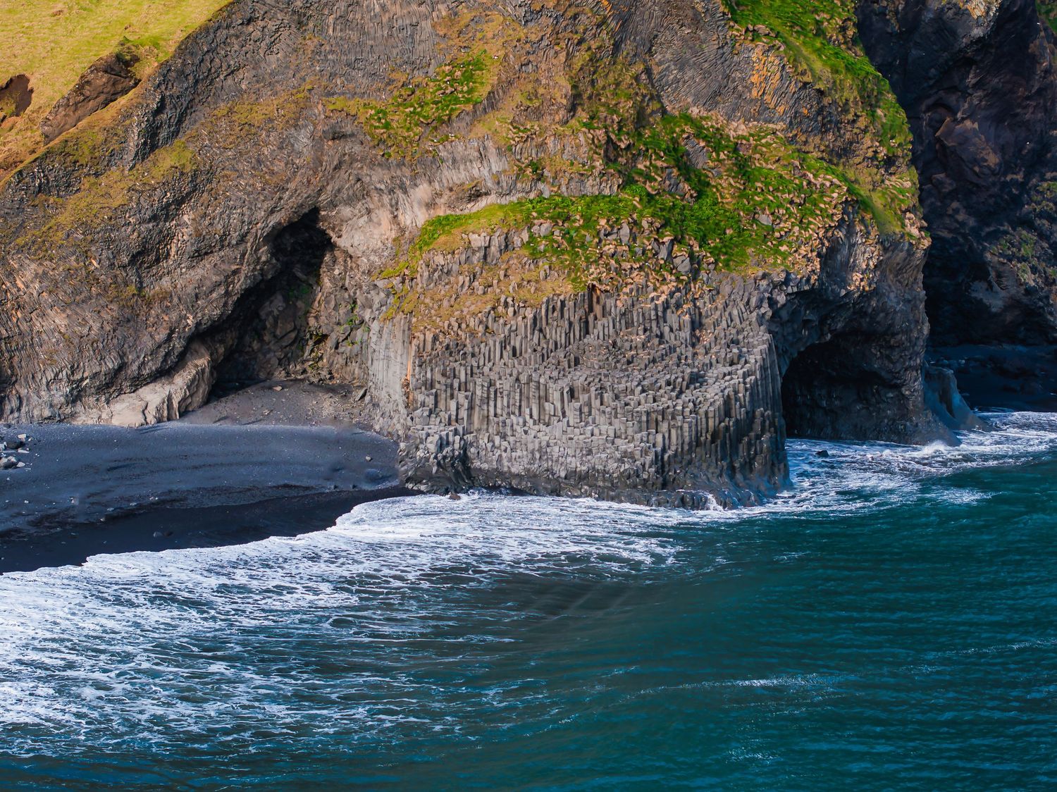 Coastal waterfall plunges dramatically into turquoise ocean waters along rugged cliff face.
