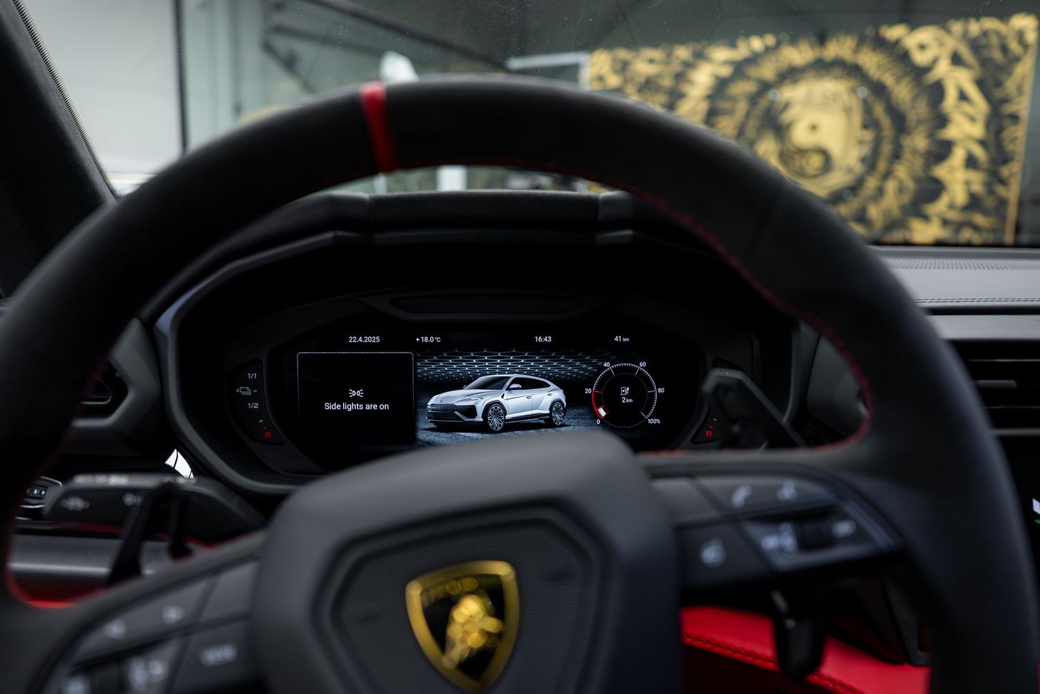 Lamborghini digital dashboard display showing vehicle silhouette behind steering wheel with logo.