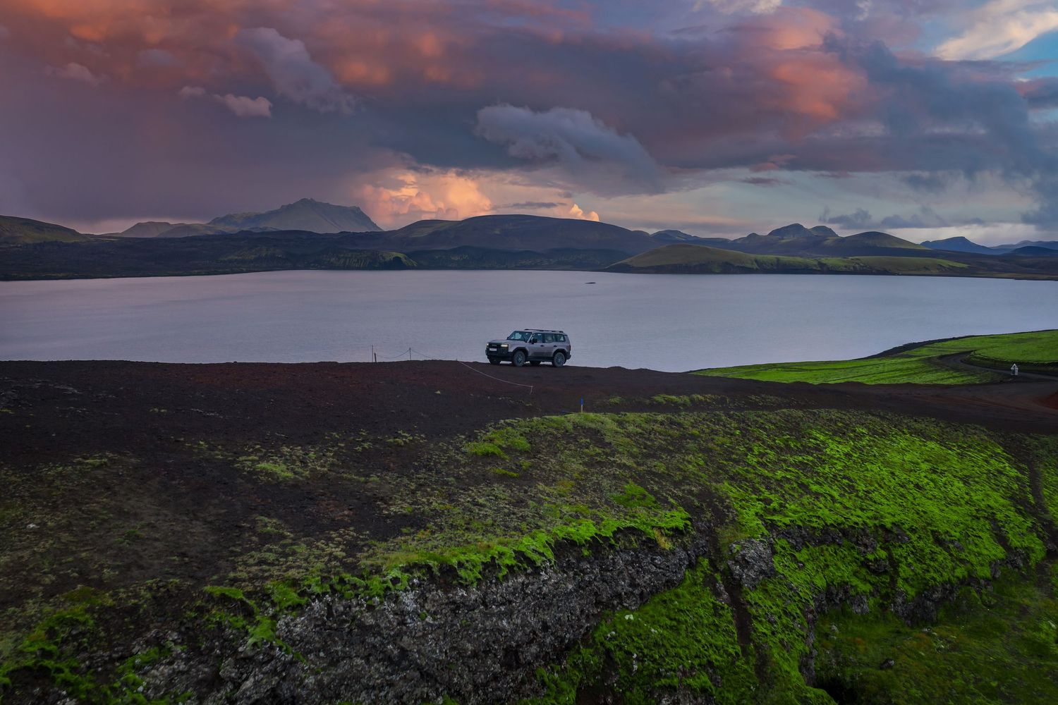 A stunning panoramic view of rolling green hills against a dramatic sunset sky with scattered clouds.
