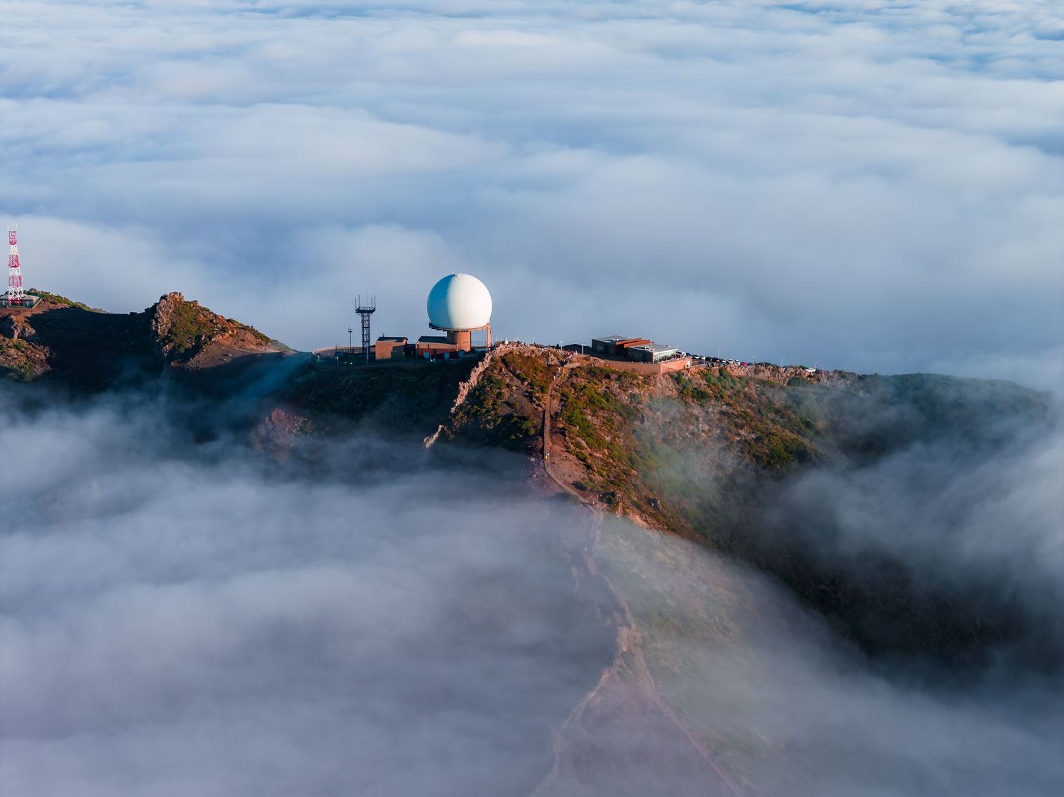 Dramatic aerial view of fog rolling over coastal cliffs with a lighthouse perched on the rocky headland.