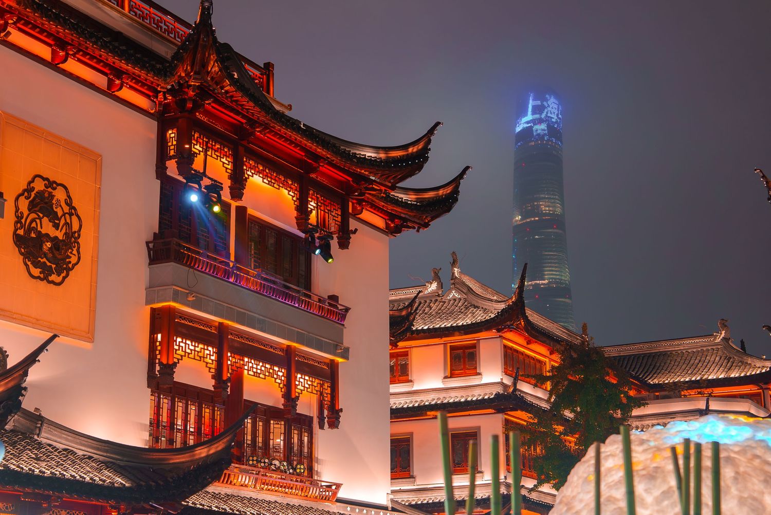 Traditional Chinese temple architecture with modern skyscrapers visible in background at night.