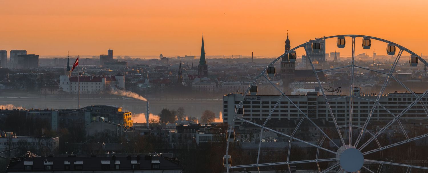 Dramatic orange and pink sunset sky over a city skyline with silhouetted buildings and a Ferris wheel.