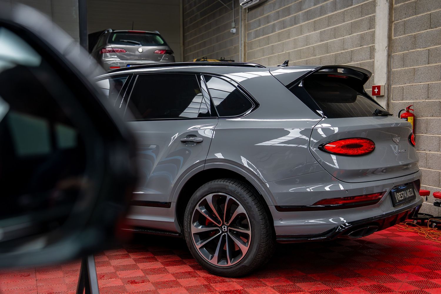 Side profile view of a gray Bentley luxury vehicle in a showroom setting.
