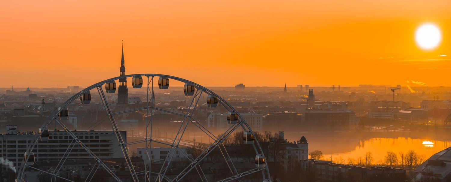 Dramatic orange sunset panorama over a city skyline with silhouetted buildings and industrial structures.