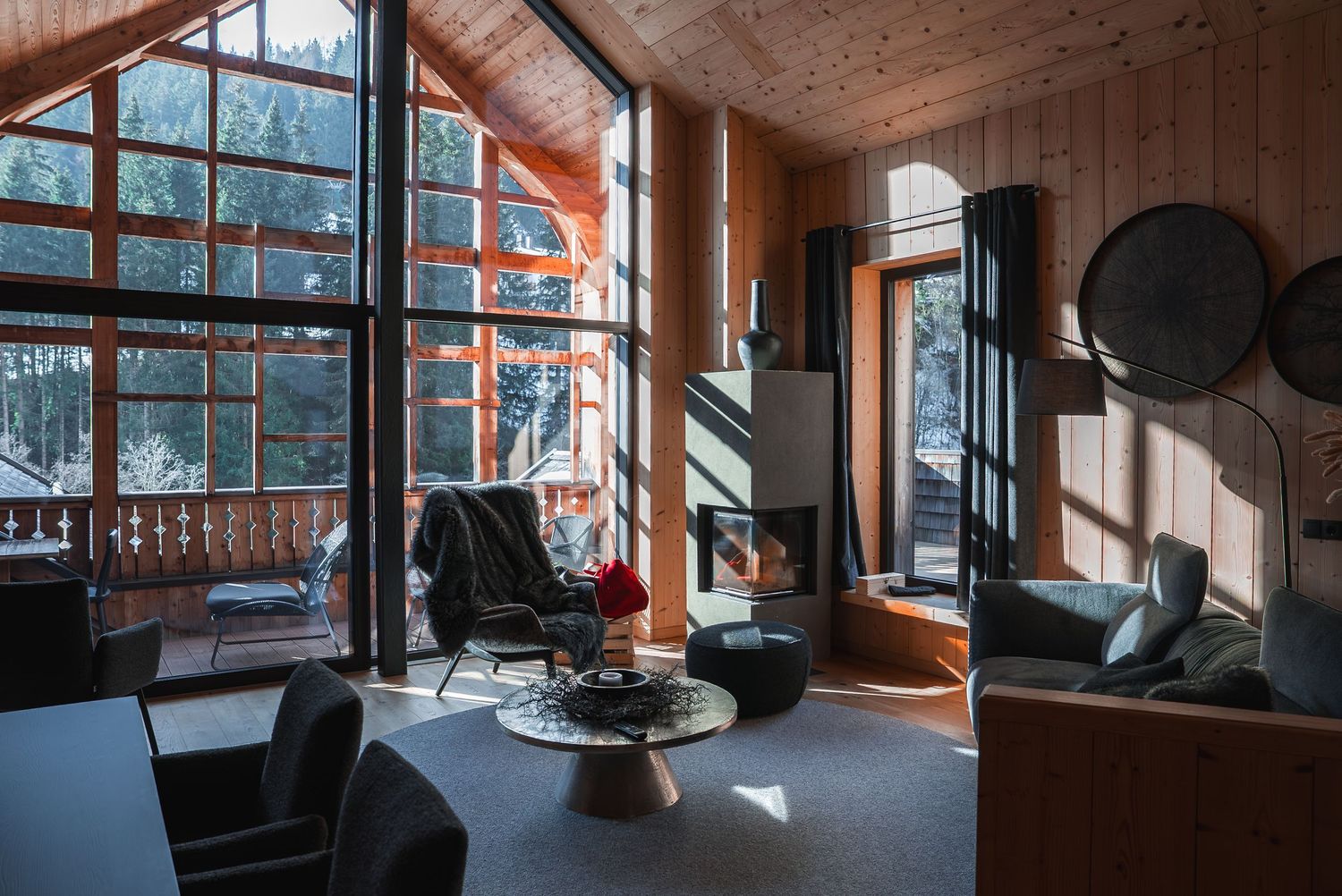 Mountain lodge interior with panoramic windows overlooking snowy forest landscape.