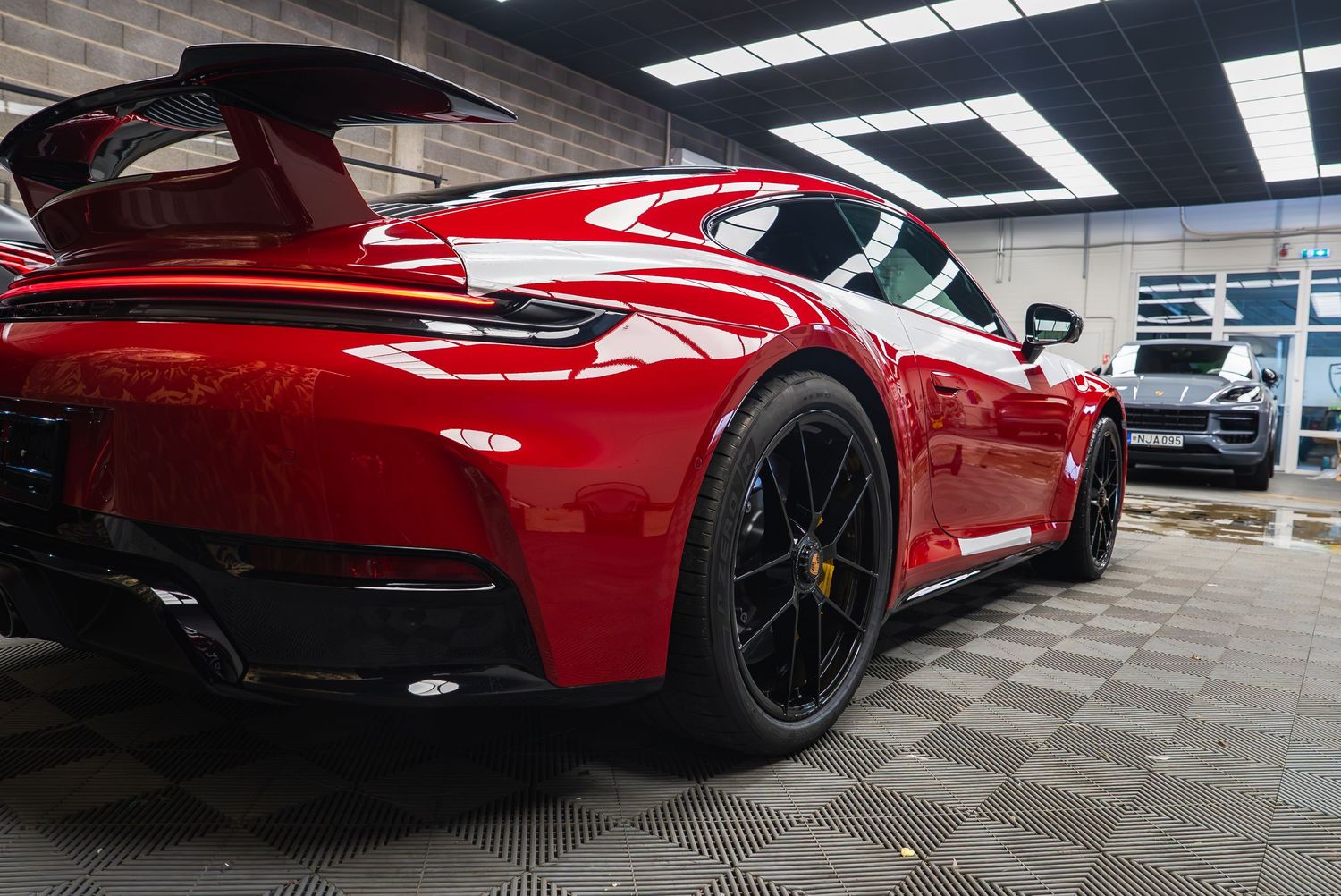 Red Porsche sports car rear quarter view with black wheels on checkered floor.