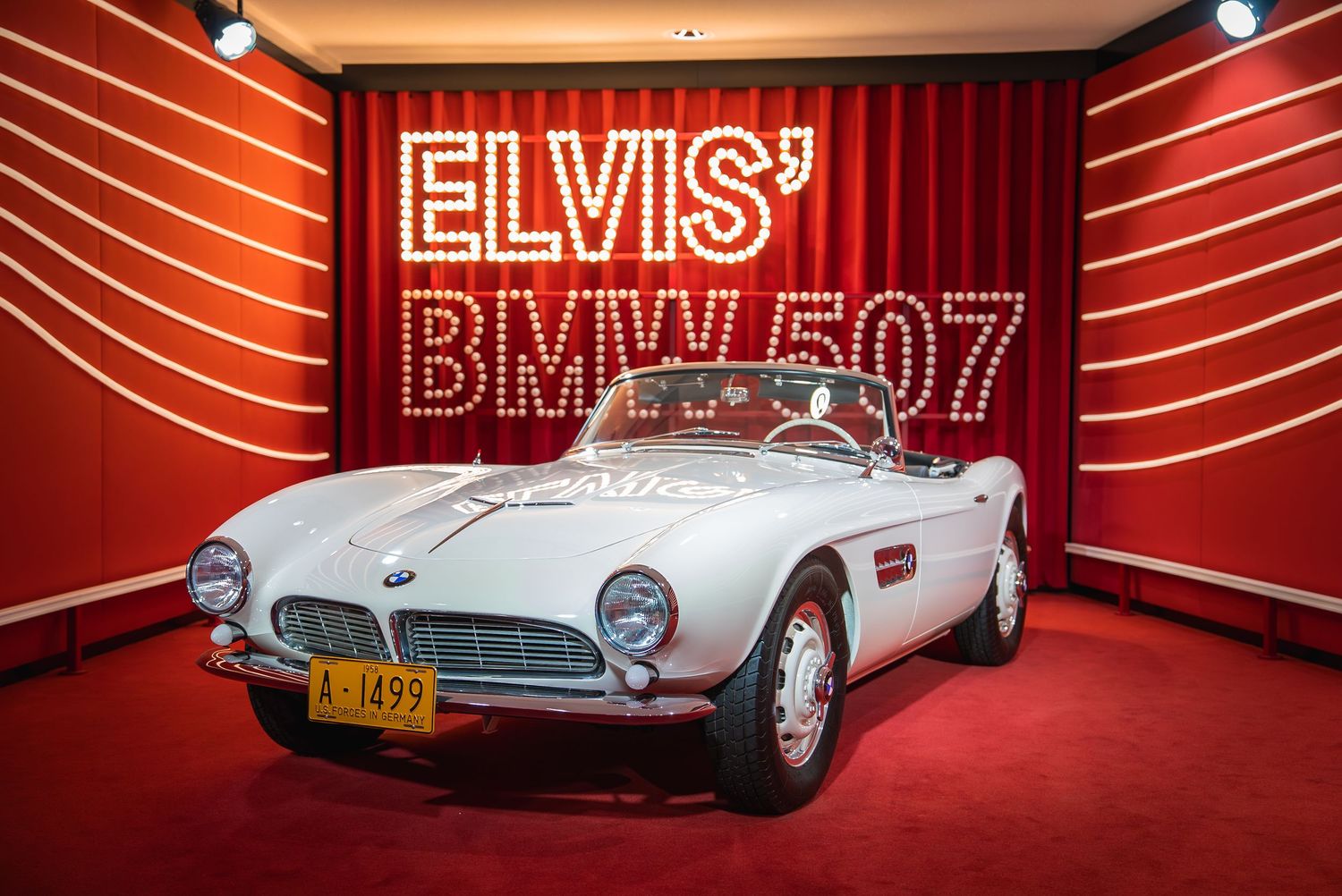 Classic cars displayed in a red-lit automotive museum exhibition space.