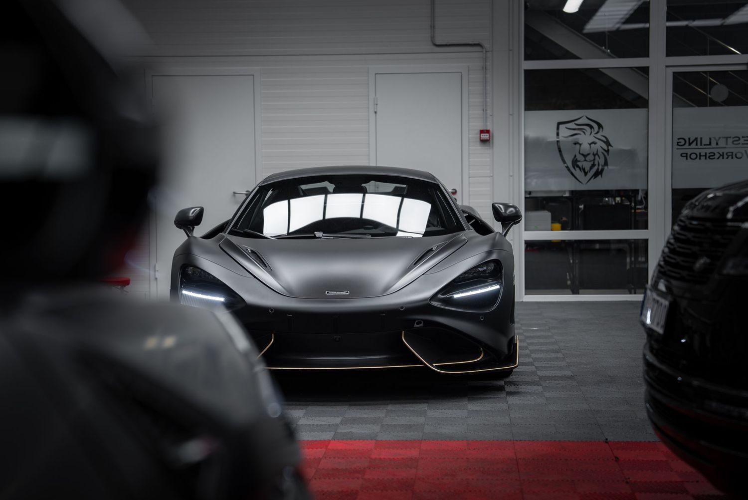 Luxury sports cars lined up in dimly lit showroom with dramatic shadows.