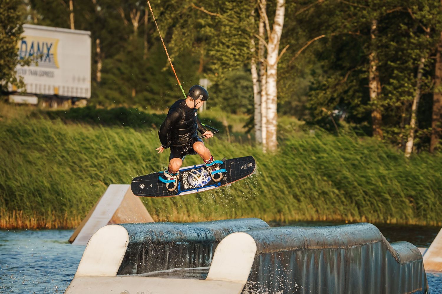 Wakeboarder performing aerial trick off ramp at sunset on lake.