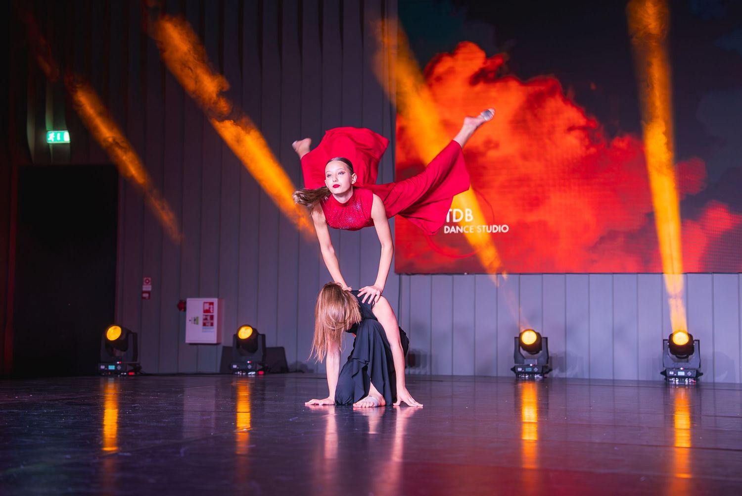 Dramatic performance on stage with orange spotlights and silhouetted dancers.