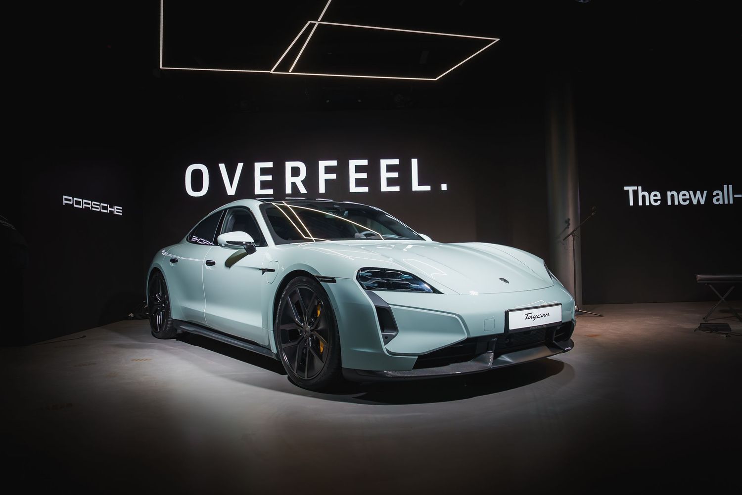 Light blue Porsche electric vehicle on display at an auto show with Overfeel branding.