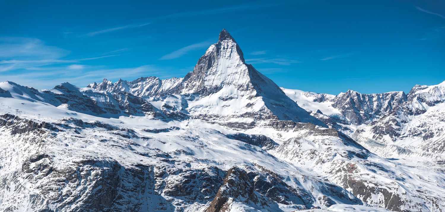 Panoramic winter landscape of snow-covered Alpine mountains with dramatic peaks against blue sky.