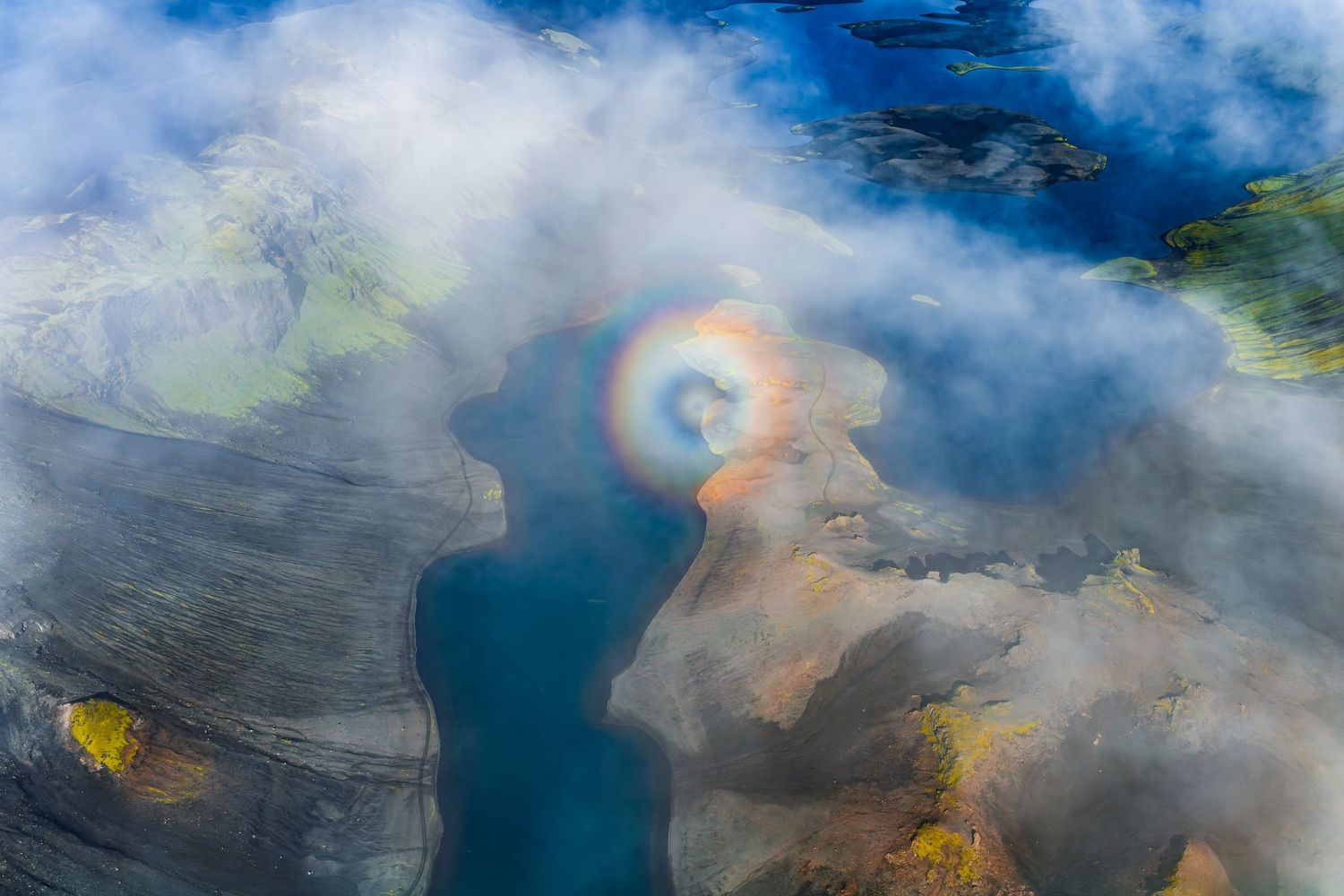 Aerial view of vibrant geothermal hot springs with turquoise blue water and steam rising against cloudy sky.