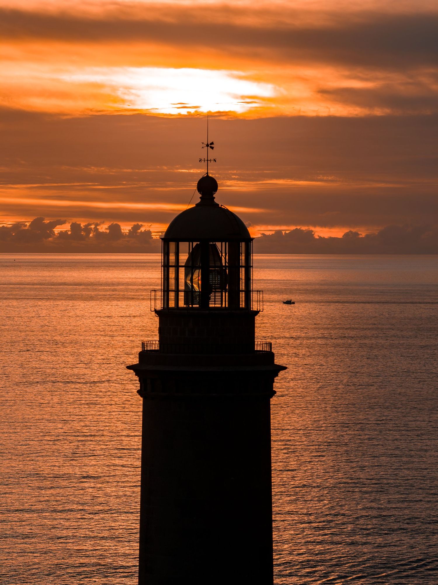Dramatic silhouette of a lighthouse against a vibrant orange sunset sky over the ocean.