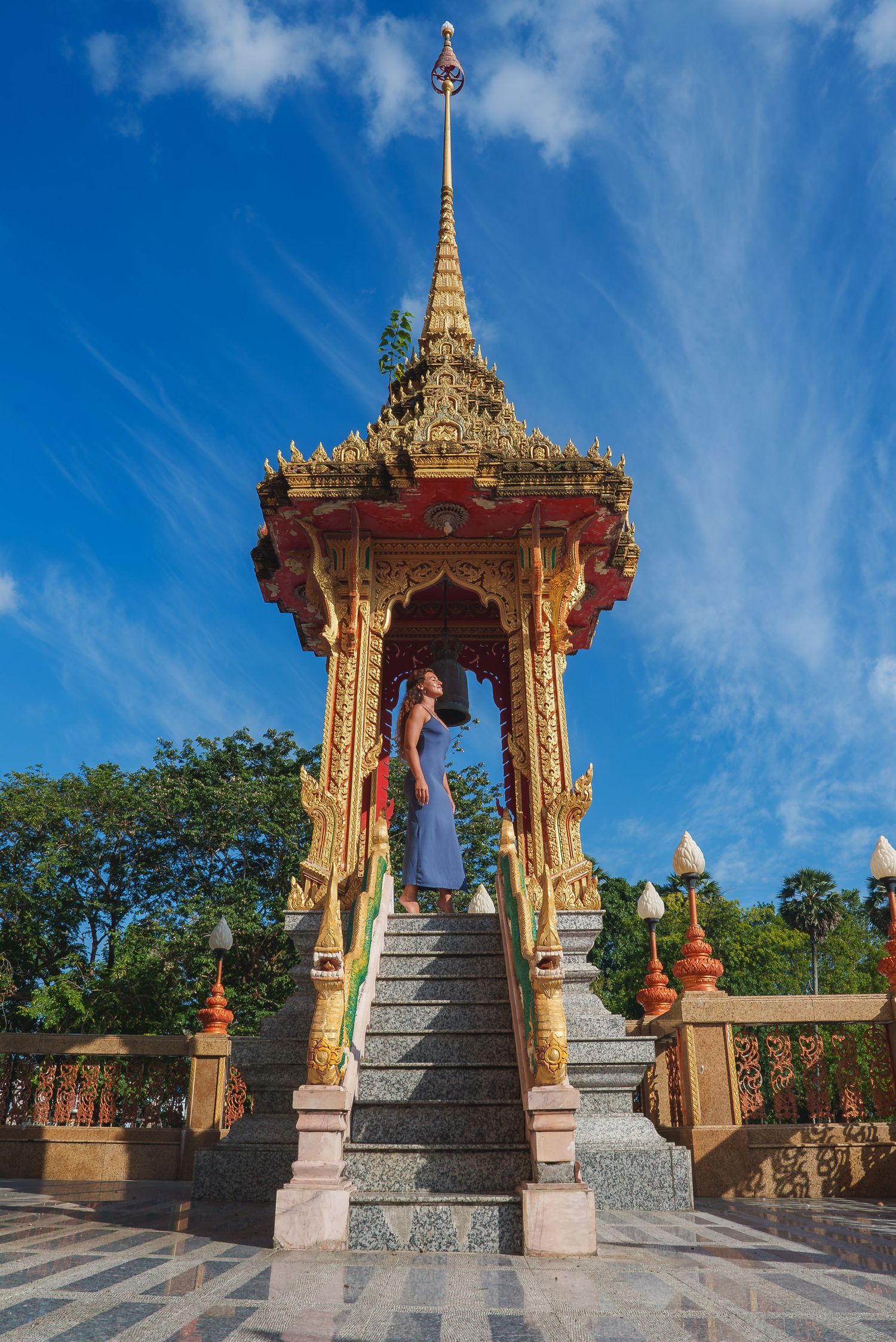 Golden Buddhist temple stairs leading to ornate shrine against bright blue sky with white clouds.