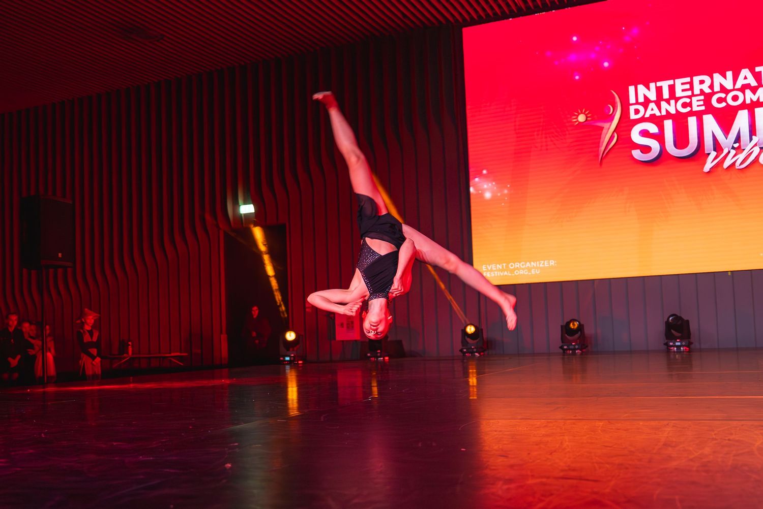 Dance competition stage lit with dramatic red and orange lighting effects.