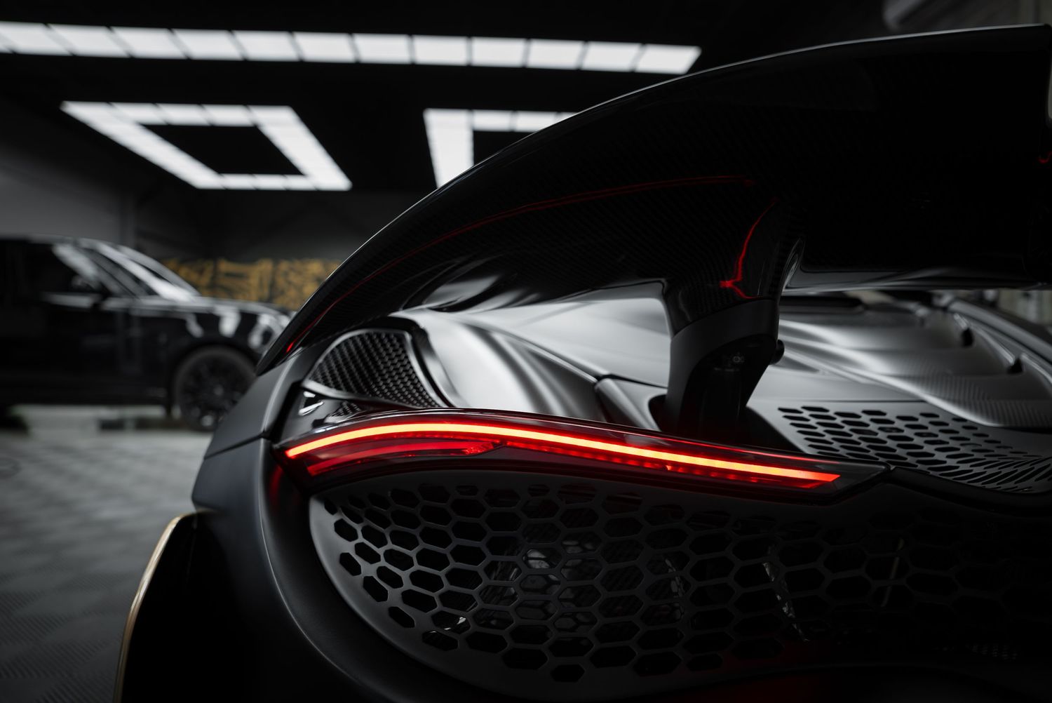 Dramatic close-up shot of a sleek black supercar's front end with LED headlights in a dark garage setting.