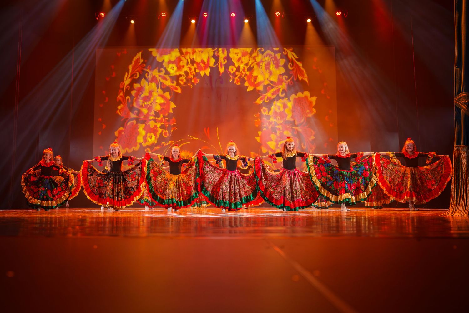 Dancers perform on stage with dramatic orange lighting and theatrical smoke effects in a dynamic show sequence.