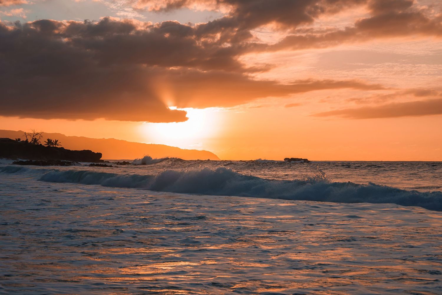 Dramatic ocean sunset with orange sky and silhouetted coastline reflecting on calm waters.
