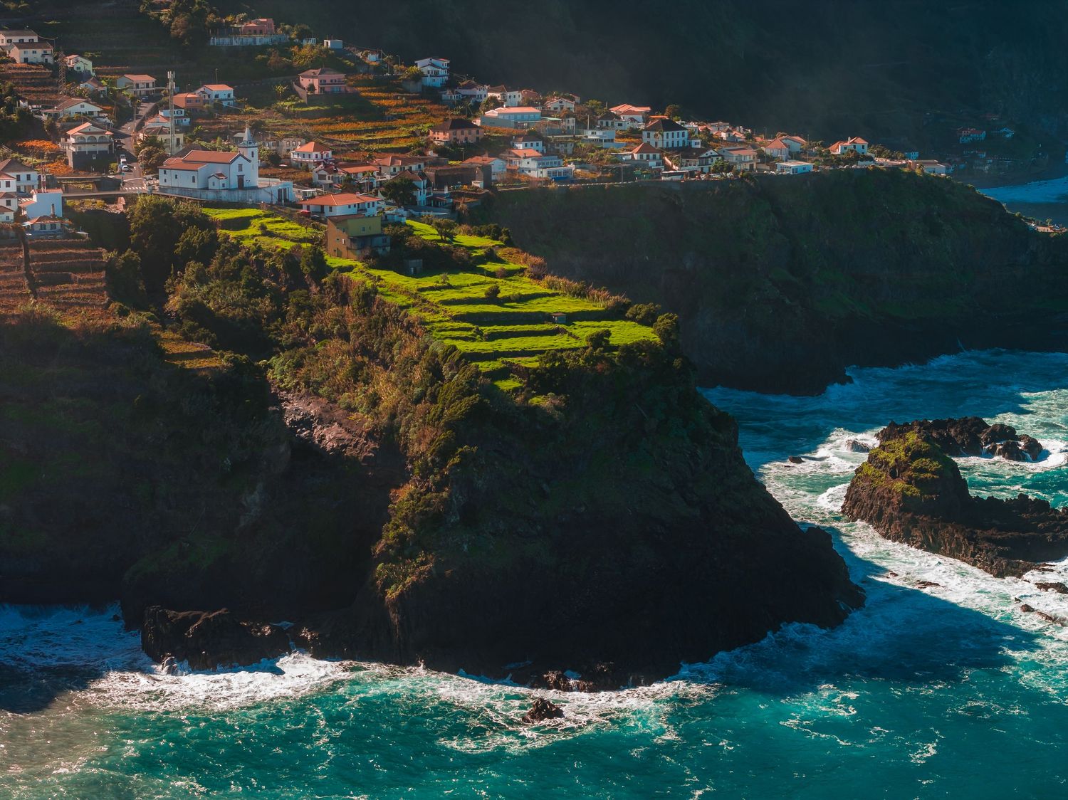 Aerial view of colorful coastal village buildings perched on cliffs overlooking the turquoise ocean waters.