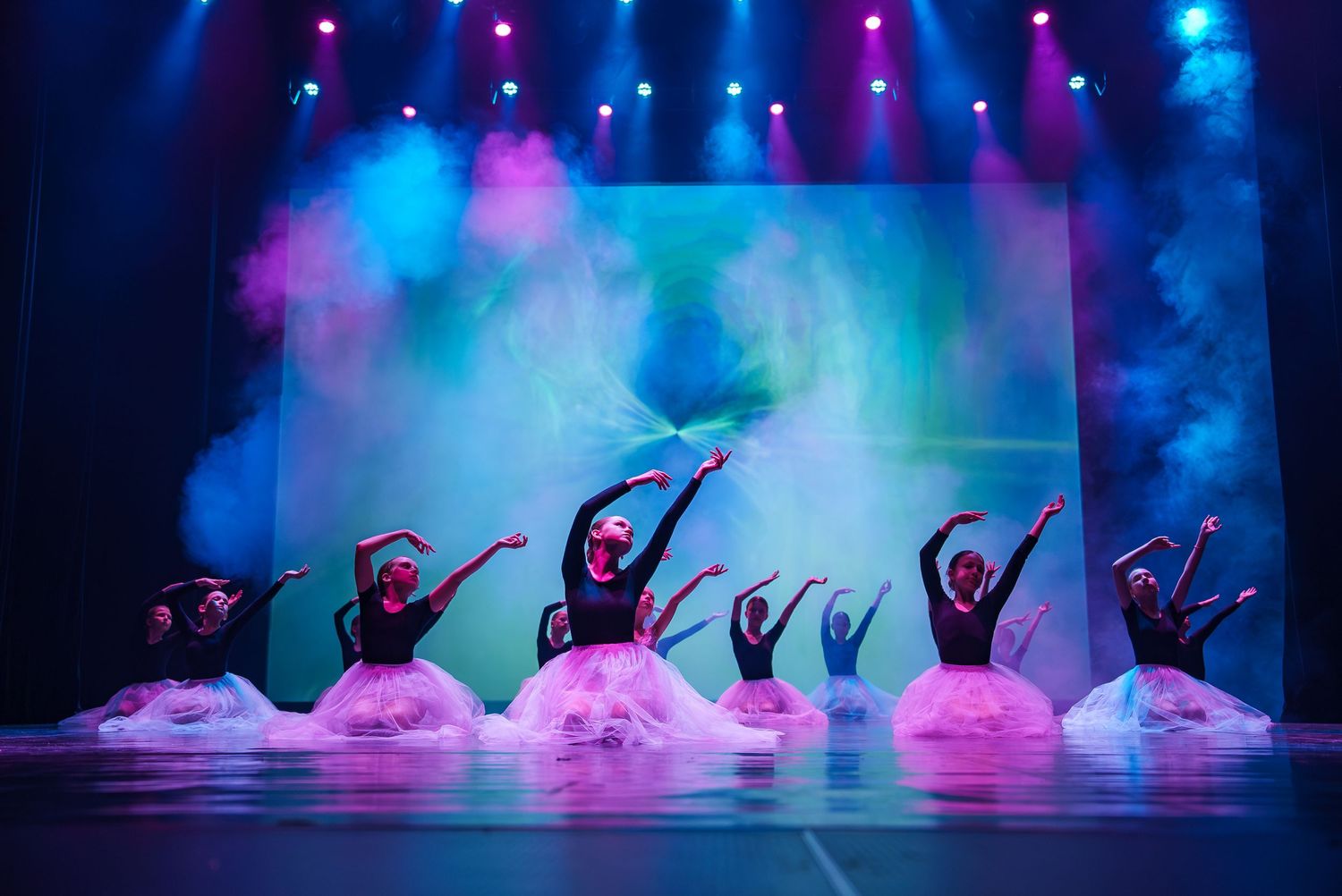 Silhouetted dancers performing on stage with colorful smoke and lighting effects.