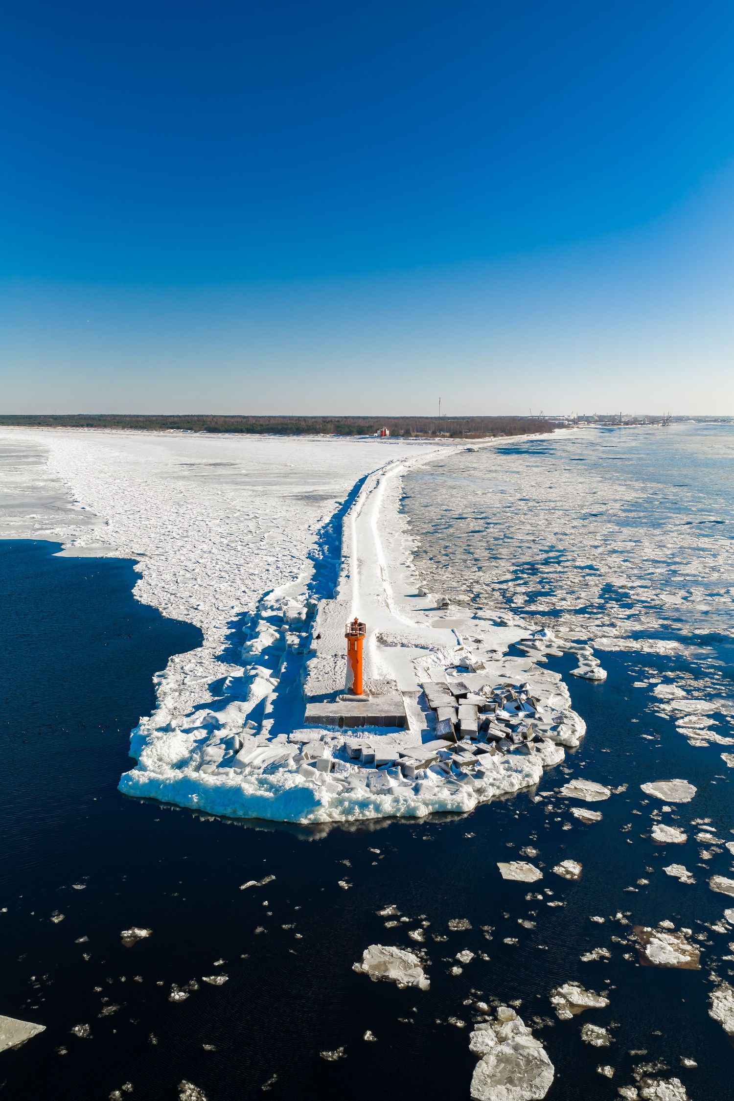 A bright orange lighthouse stands tall on a snowy shoreline surrounded by frozen ice floes in Lake Michigan.