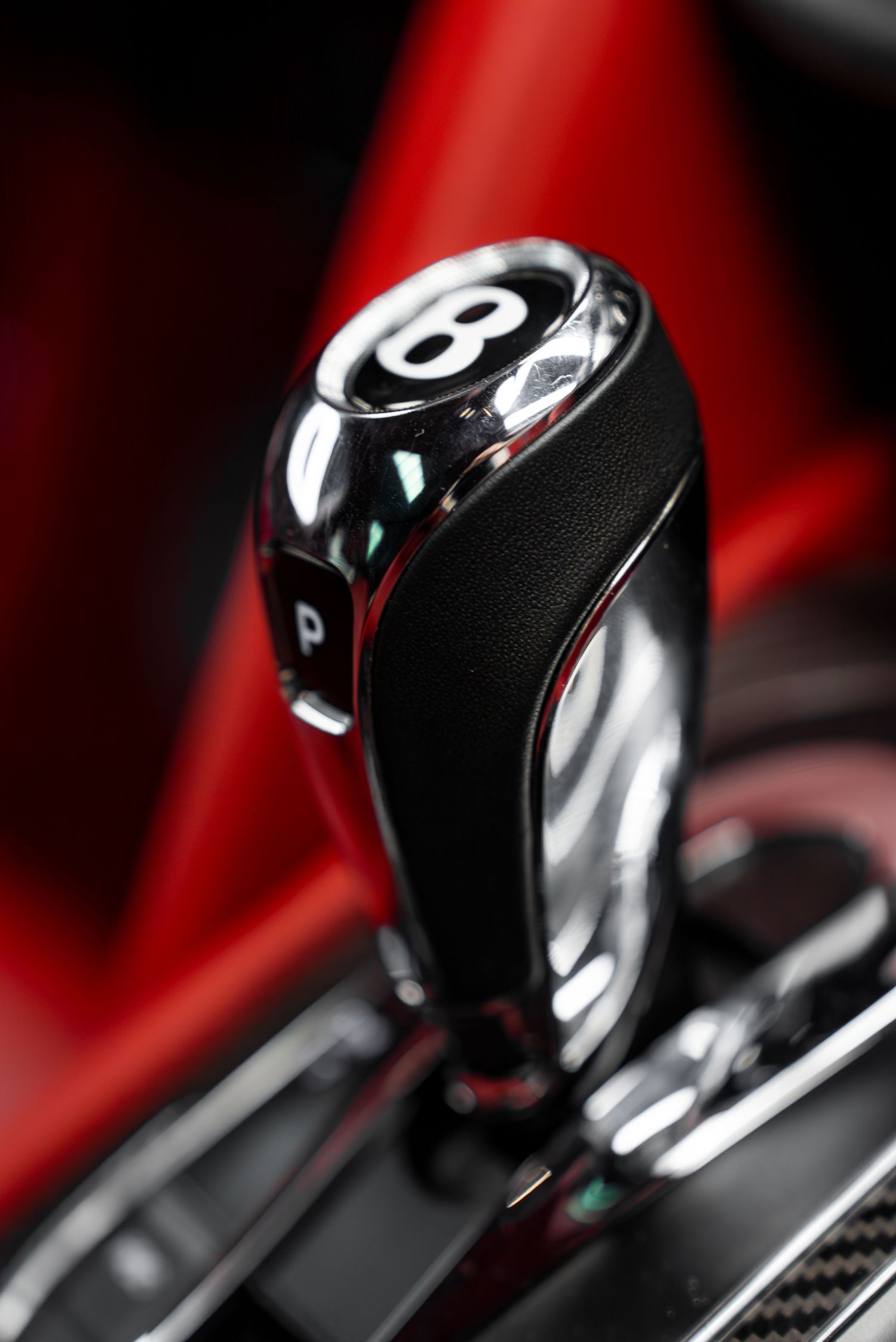 Close-up of luxury car gear shifter with number 8 on black and red background.