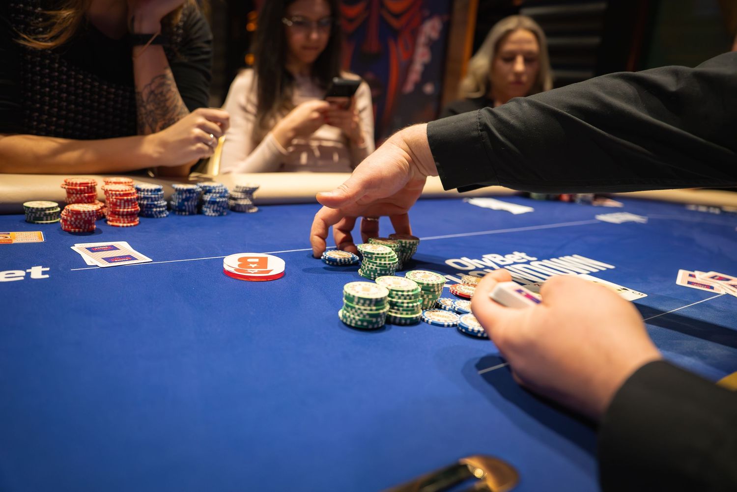 Players placing bets with poker chips on a blue felt gaming table.